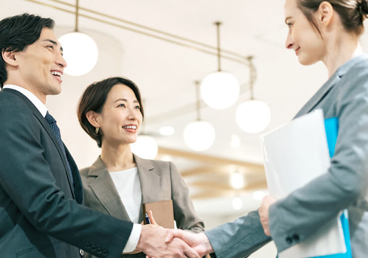 写真：海外の顧客と笑顔で握手する日本のビジネスマンとビジネスウーマン